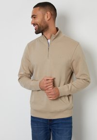 Sweatshirt beige à demi-zip en tissu doux, avec manches longues, bords côtes aux poignets et à l'ourlet, et poches latérales. Design simple et minimaliste.