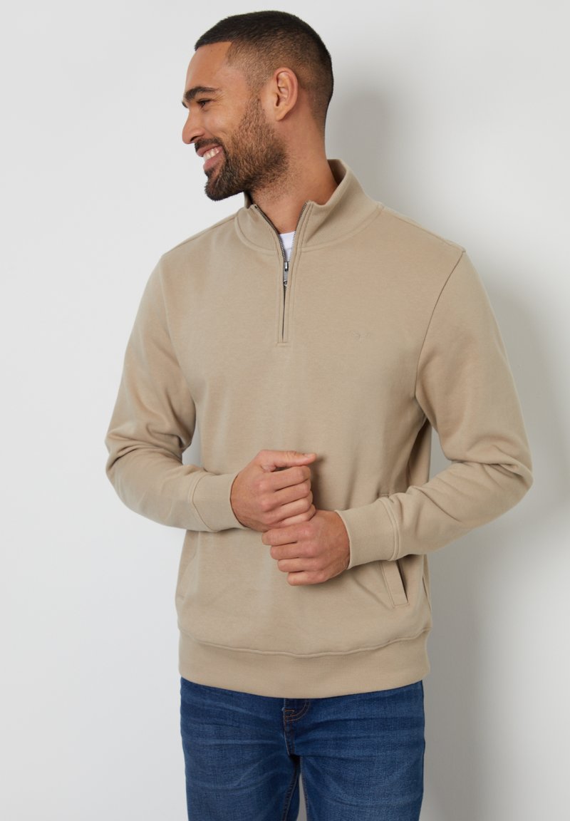 Sweatshirt beige à demi-zip en tissu doux, avec manches longues, bords côtes aux poignets et à l'ourlet, et poches latérales. Design simple et minimaliste.