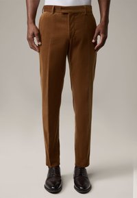 Bruine korduroybroeken met rechte pijpen, zijzakken en een vlakke voorkant, gecombineerd met zwarte leren schoenen. Glad textuur, op maat gesneden pasvorm.