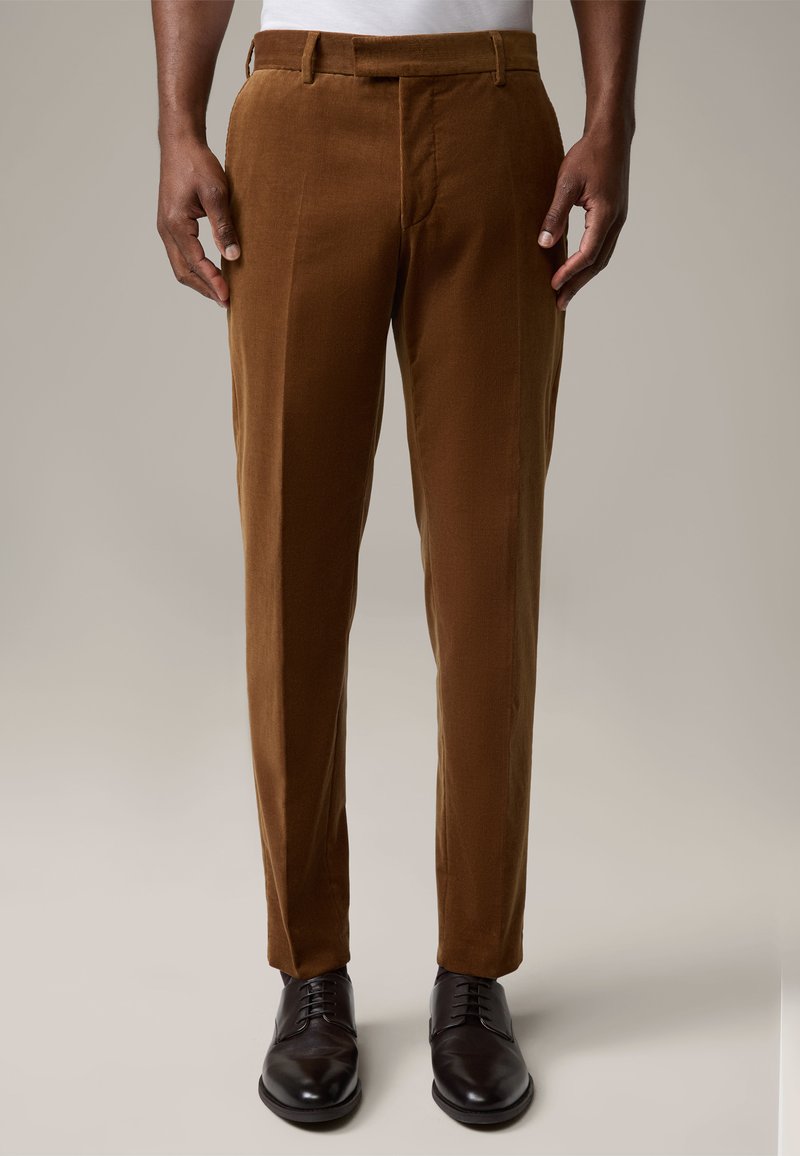Braune Baumwollcord-Hosen mit geraden Beinen, seitlichen Taschen und flachem Bund, kombiniert mit schwarzen Lederschuhen. Glatte Textur, maßgeschneiderte Passform.