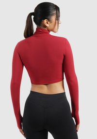 Rode cropped top met lange mouwen en hoge kraag, gemaakt van glad, rekbaar materiaal. Gekozen met zwarte high-waisted legging.