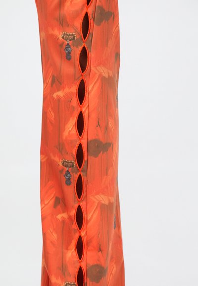 Oranžs audums ar rakstu un gludu tekstūru, aksentēts ar izgriezumiem sānos un kontrastējošām oranžām šuvēm.