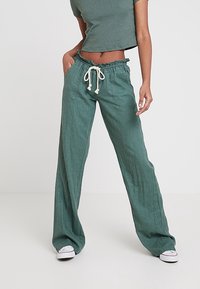 Groene linnen wijde broek met elastische tailleband, trekkoordsluiting en twee voorzakken. Gecombineerd met een bijpassend aansluitend topje.