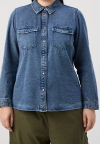 Denim shirt in dark blue with a button-down front, collar, two chest pockets, and long sleeves. Features slight fading for texture.