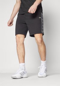 Črne kratke hlače iz mehkega blaga s prilegajočim krojem, ki imajo bele stranske črte z ponovljenim tiskom logotipa in majhen zeleni logotip spredaj.