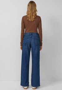 Szerokie, ciemnoniebieskie dżinsy z wysokim stanem, zestawione z dopasowanym, brązowym, długim rękawem. Materiał ma gładką, dżinsową fakturę. Widać dwie tylne kieszenie.