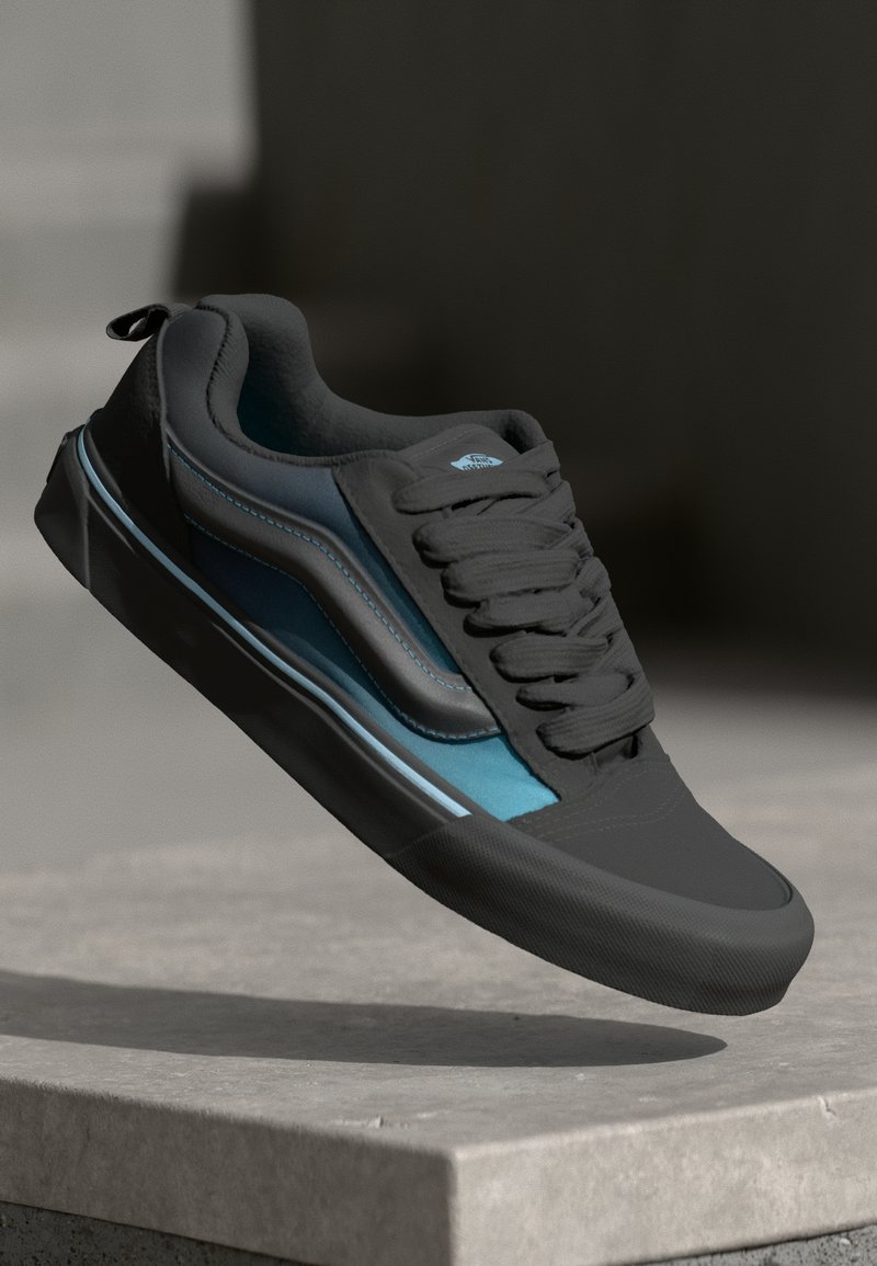 Zwarte en teal sneaker van een glad materiaal, met een ronde neus, een gestructureerde rubberen zool en een opvallend vetersysteem.