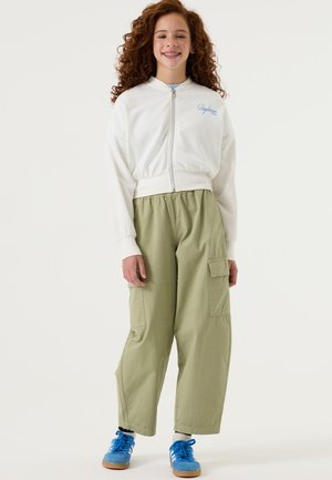 Chaqueta bomber blanca con cremallera, pantalones cargo verde claro con bolsillos laterales, zapatos deportivos azules, con una textura suave y un ajuste relajado.