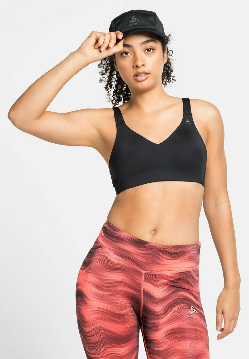 Zwarte sportbeha met een v-halsontwerp, gecombineerd met gekleurde, aansluitende roze leggings met golvende lijnen en een logo op de tailleband.