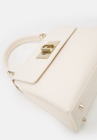 Kremowa torebka z teksturowanej skóry, o strukturalnym prostokątnym kształcie, z złotymi akcentami i detalami na podstawie dla stabilności.