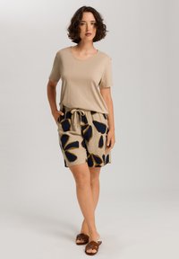 Beige Kurzarmshirt kombiniert mit hellbeigen Shorts, die ein dunkelblaues Blumenmuster und einen Kordelzugbund haben. Braune flache Sandalen sind enthalten.