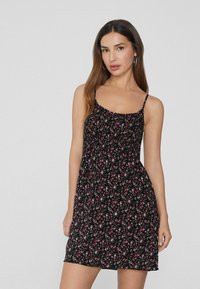 Schwarzes Blumenkleid mit schmalen Trägern, ausgestattet mit einem gerafften Oberteil und einem schwingenden Rock, der mit kleinen rosa und weißen Blumen verziert ist.