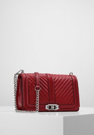 Punainen tikattu nahkainen käsilaukku, jossa on hopeinen ketjuhihna ja suorakaiteen muotoinen hopeinen lukko, esillä valkoisella pinnalla yksiväristä taustaa vasten.