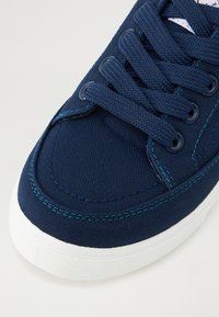 Sneaker bleu marine foncé avec tige en toile texturée, lacets plats et coutures turquoise contrastantes. Semelle extérieure en caoutchouc blanche avec une surface à motif.