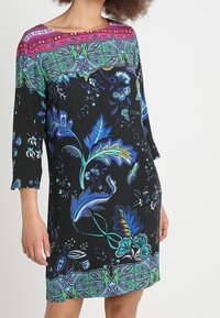 Svart klänning med trekvartsärmar, prydd med ett färgstarkt mönster av blommor och paisley, med en livlig flerfärgad detaljer vid halsringningen.