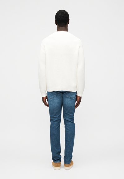 Roomkleurige gebreide trui met een ontspannen pasvorm, gecombineerd met blauwe rechte jeans en beige sneakers. Minimalistisch design en gestructureerde stof.