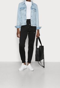 Ljusblå denimjacka, vit t-shirt, svarta joggers med dragsko, vita sneakers och svart tote bag. Släta texturer och avslappnad passform.