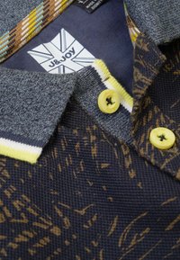 Polo shirt is voorzien van een grijze kraag, gele knopen en een marineblauwe body met een gestructureerd bruin patroon. Bevat een logolabel aan de binnenkant van de kraag.