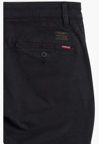 Poche arrière d'un pantalon Levi's noir avec fermeture à bouton, étiquette logo Levi's rouge et patch en cuir noir avec texte de la marque.