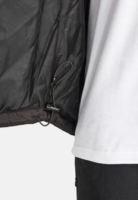 Giacca a vento nera con superficie testurizzata, cordoncino regolabile all'orlo e una camicia bianca a contrasto sottostante.