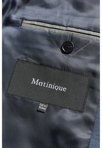 Must Mustique brändi silt ja suurusetikett (EUR 50, USA 40) tumedasinise ülikonna voodri sees musta nööbi ja halli detailiga.