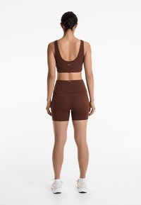 Brown athletic set featuring a ribbed crop top with wide straps and high-waisted shorts, showcasing a smooth material and fitted design.