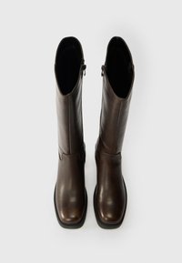 Botas de couro castanhas até ao joelho com um acabamento liso, bicos apontados, fechos laterais e uma sola de borracha para tração. Vista de cima.