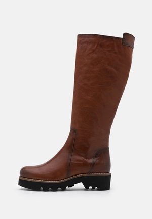 Botte haute jusqu'au genou en cuir marron avec un bout arrondi, une surface texturée, un léger éclat, et une semelle noire en caoutchouc à crampons. Coutures détaillées le long des bords.