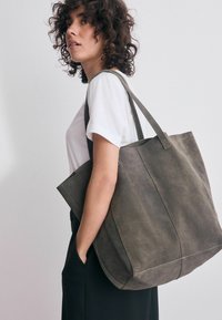 Olivgrön kordtovedsväska med stabila remmar, rektangulär form och texturerad yta, bärs över axeln med sidofickdetalj.
