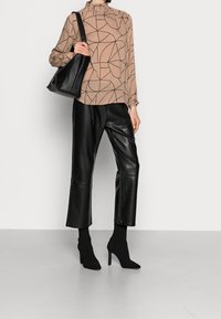 Blouse beige avec motif géométrique noir, col volanté ; pantalon d'effet cuir noir, bottines pointues, et sac à bandoulière noir.