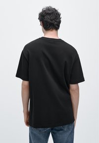 Black short-sleeve t-shirt made of cotton. Features a crew neck and a relaxed fit, with visible stitching details on the sleeves.