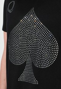 Camiseta negra con un gran gráfico de strass plateado en forma de trébol, acompañado de un pequeño detalle circular arriba.