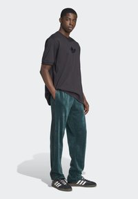 Černé tričko s krátkým rukávem s tónovým logem; tyrkysové sametové kalhoty s černými pruhy po stranách; černé tenisky s bílými pruhy.