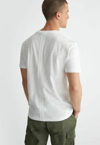 T-shirt bianco a maniche corte con collo rotondo, dotato di una cucitura centrale sul retro. Il tessuto presenta una leggera trama. Abbinato a pantaloni cargo color oliva.