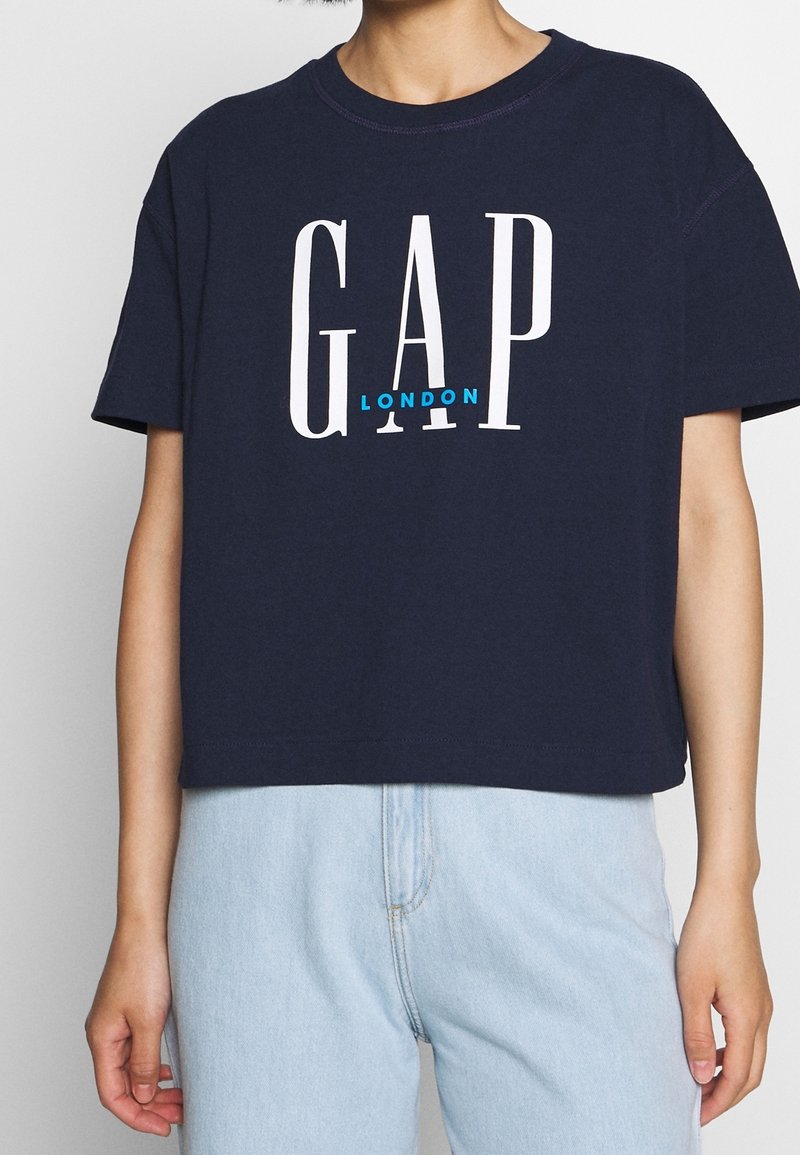 T-shirt coupe courte bleu marine en coton, avec un grand lettrage blanc "GAP" et un plus petit "LONDON" en turquoise en dessous.