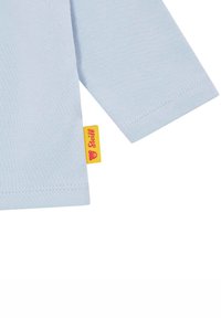 Himmelblaues Langarmhemd mit glatter Textur. Verfügt über ein kleines gelbes Etikett mit rotem Logo und einer genähten Saum.