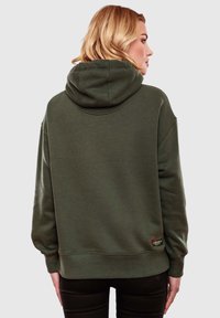 Sudadera verde oliva con superficie texturizada, corte holgado y capucha. Presenta puños y dobladillo de canalé con un parche de logo en la cintura.