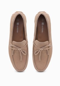 Hnědé semišové loafers s kulatou špičkou, jemnou texturou a středovým mašlí. Nazouvací styl s hladkým vnitřním podšívkou.