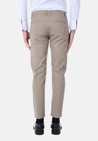 Chinos beige con una vestibilità slim, dotati di tasche posteriori e passanti per cintura. Indossati con una camicia bianca e scarpe nere. Tessuto a superficie liscia.