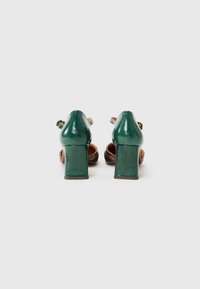 Green patent leather high heel shoes with square block heels, adjustable ankle straps, and rounded toe design. Features a smooth texture.