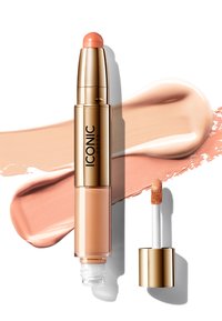 Parkerosa kremmakeup-stick med en gullfarget tube, ledsaget av en dobbeltsidig applikator med svampetupp og doe-foot-tupp.