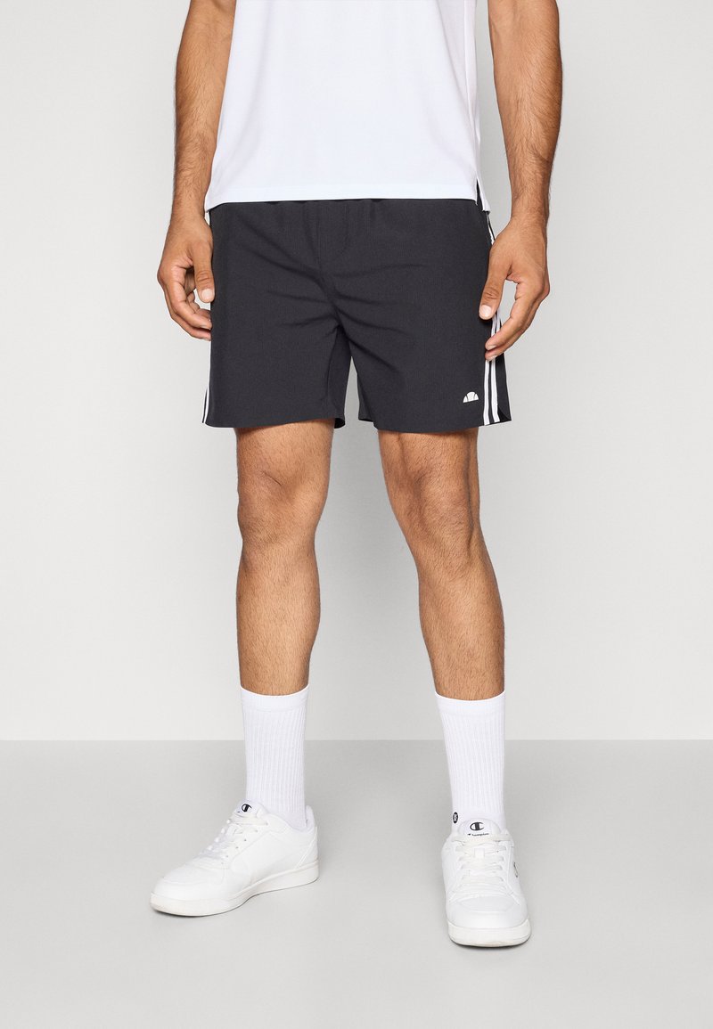 Pantalones cortos deportivos negros con una textura suave, que presentan dos franjas laterales blancas y un pequeño logo en la parte inferior izquierda. Llevados con calcetines blancos y zapatillas deportivas.