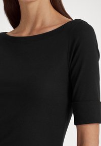 Svart topp med båtringning, korta ärmar med uppvikta muddar och en slät, åtsittande textur.