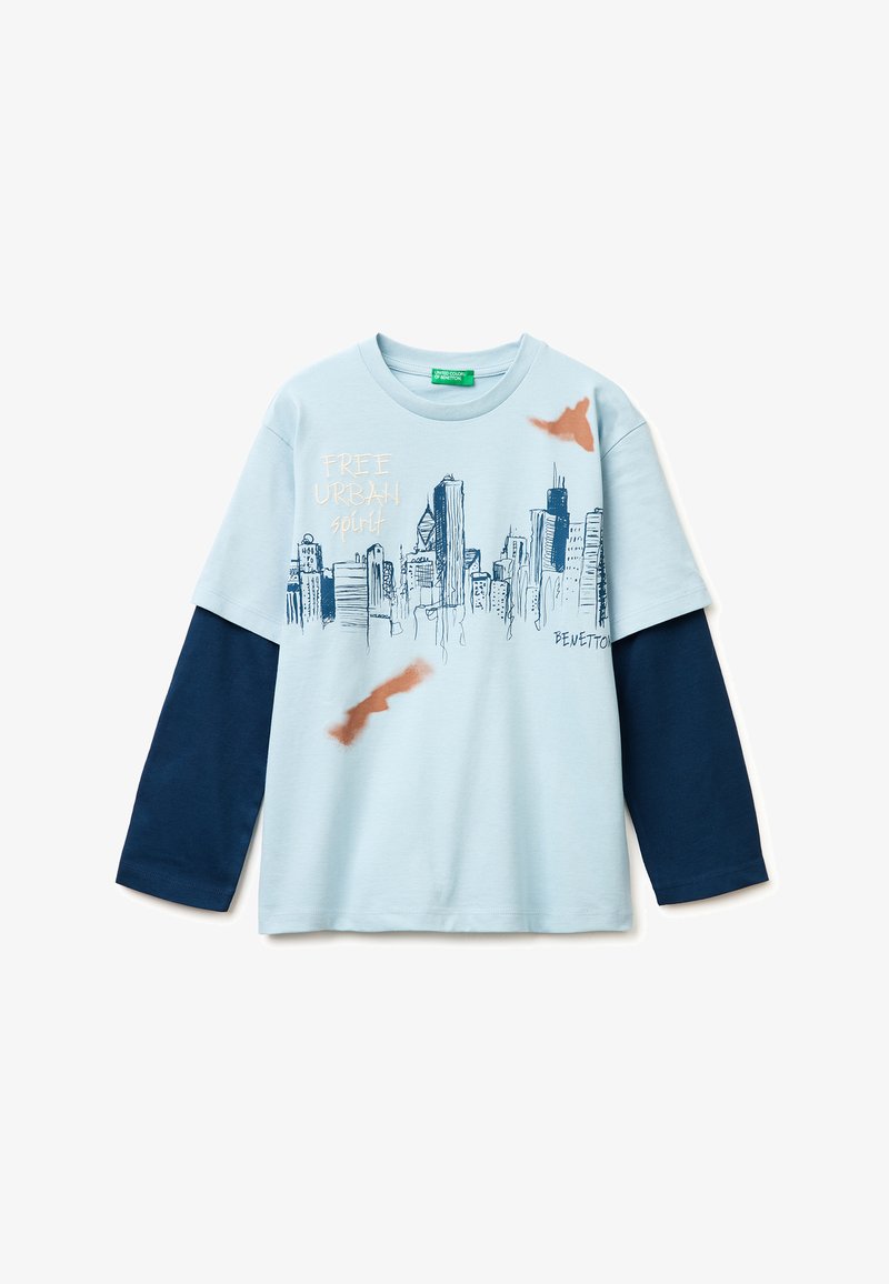 Camisa de manga larga azul celeste con mangas azul marino, gráfico de horizonte de la ciudad en azul marino, texto "FREE URBAN spirit" y pequeñas salpicaduras de pintura naranja.