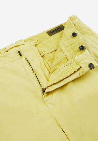 Pantaloni di cotone gialli con zip, chiusura a bottone e dettagli cuciti. La texture del tessuto sembra liscia con una leggera lucentezza.