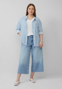 Jasnoniebieska i biała, paskowana koszula zapinana na guziki, biała koszulka z dekoltem w serek, szerokie jasnoniebieskie dżinsy oraz białe sportowe buty wsuwane.