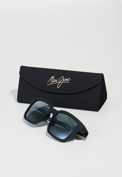 Ochelari de soare Maui Jim negri, cu finisaj mat, lentile pătrate cu nuanță gradient, poziționați lângă un toc elegant negru, decorat cu un logo auriu.