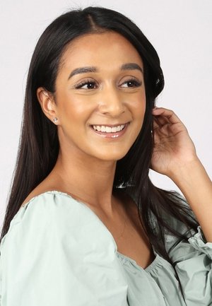 Lichtgroene off-shoulder blouse met elastische halslijn en pofmouwen. Lang, donker haar, natuurlijke make-up en zichtbare oorbellen. Helde achtergrond.