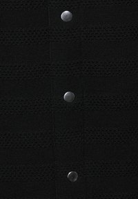 Czarna dzianina z teksturowanymi paskami oraz pięcioma okrągłymi srebrnymi guzikami z przodu do zapięcia. Gładka i miękka w dotyku.