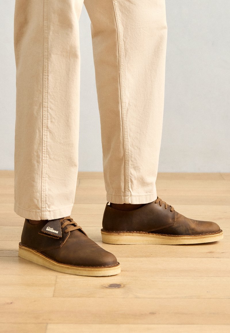 Zapatos de cuero marrón con un acabado suave, punta redondeada y suelas de goma de color claro. Acompañados por pantalones beige claros.